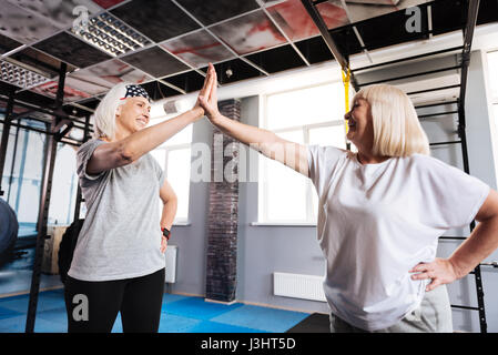 High five. Delighted positive senior women standing opposite each other and giving a high five while being in a great mood Stock Photo