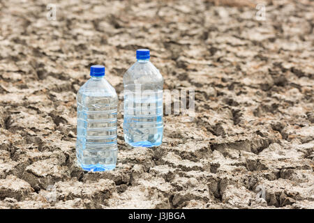 Bottle with water on the dried ground. Concept of Global drought, warming, summer. Dried soil. lack of water, thirst concept. Stock Photo