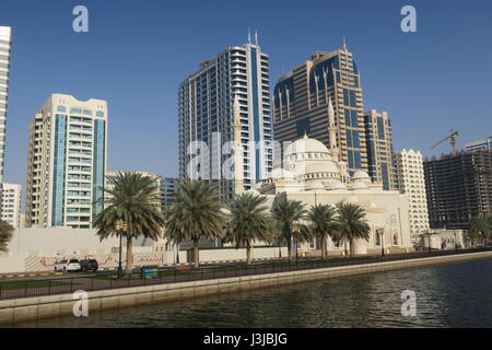 Sharjah is the third largest emirate in the United Arab Emirates. Lots of mighty skyscrapers with glass facades, palm trees, mosques. Nice garden, bay Stock Photo