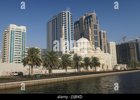 Sharjah is the third largest emirate in the United Arab Emirates. Lots of mighty skyscrapers with glass facades, palm trees, mosques. Nice garden, bay Stock Photo