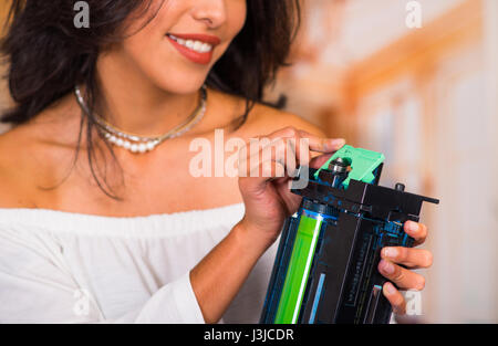 Closeup of a beautiful woman fixing a photocopier and smiling during maintenance repairs using handheld tool. Stock Photo