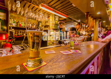 BRUSSELS, BELGIUM - 11 AUGUST, 2015: Glass of beer sitting on bar counter inside Delirium Bar, selection of other beverages in background. Stock Photo
