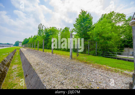 Dachau, Germany - July 30, 2015: Ditch and barbed wire fence installation around concentration camp, contrasted by beautiful green vegetation. Stock Photo