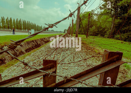 Dachau, Germany - July 30, 2015: A look through barbed wire, ditch and fence installation around concentration camp. Stock Photo