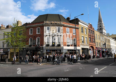 Crowd of people standing in the street in spring drinking beer outside Truman's Brewery pub The Golden Heart in Spitalfields  East London KATHY DEWITT Stock Photo