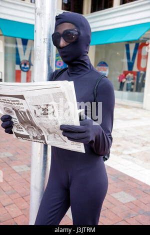 Miami Florida,Coconut Grove,street performer,busking tips,mime,dressed in black,reading,newspaper,costume,bodysuit,FL081026143 Stock Photo