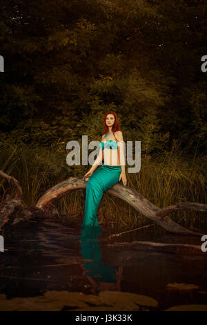 Mermaid girl sitting on a tree in the swamp. Stock Photo