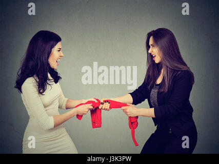 two greedy women fighting for red tank-top on gray wall background Stock Photo