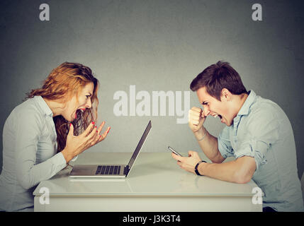 Stressed business woman with laptop sitting at table with angry man screaming at mobile phone. Negative emotions in office life Stock Photo