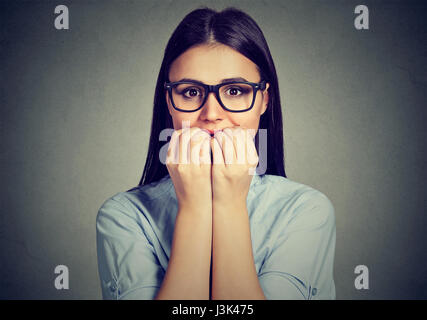 Closeup portrait unsure hesitant woman biting her fingernails craving for something or anxious isolated on gray wall background. Negative human emotio Stock Photo