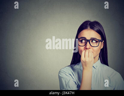 Closeup portrait unsure hesitant woman biting her fingernails craving for something or anxious isolated on gray wall background. Negative human emotio Stock Photo