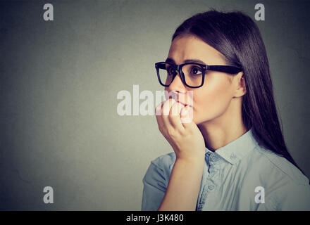 Closeup portrait young unsure hesitant woman biting her fingernails craving for something or anxious isolated on gray background. Negative human emoti Stock Photo