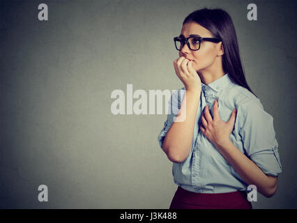 Closeup portrait unsure hesitant woman biting her fingernails craving for something or anxious isolated on gray wall background. Negative human emotio Stock Photo