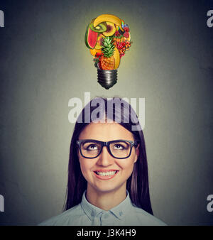 Eating healthy diet tips concept. Headshot of a woman looking up at light bulb made of fruits isolated on gray wall background. Stock Photo