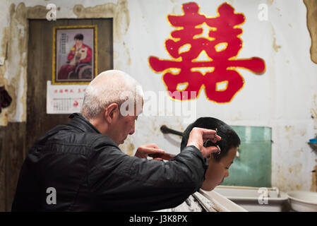 GaoMao Ancient village, Meishan, Sichuan Province, China - Apr 29, 2017: Man doing an haircut to a young boy in an old barbershop with the chinese 'ma Stock Photo