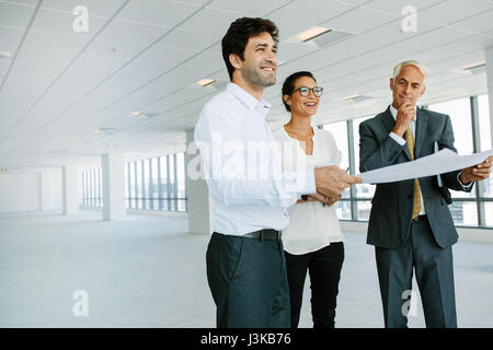 Real estate broker and business people discussing over blueprint of new office space. Real estate agent showing new office space to potential clients. Stock Photo