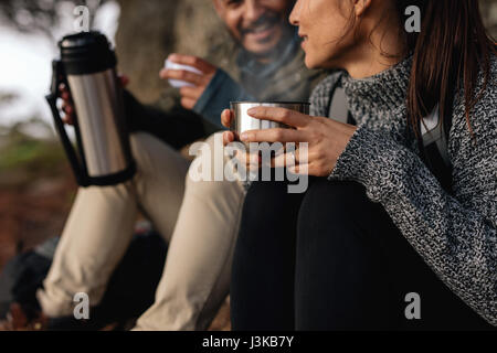 Young woman with her boyfriend taking a break on a hike. Couple hiking talking rest and drinking coffee. Stock Photo