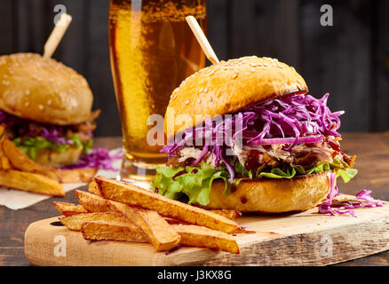 Two sandwiches with pulled pork, french fries and glass of beer on wooden background