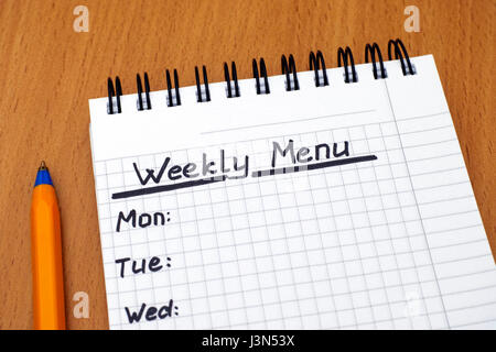 Words Weekly Menu written on white note pad with ballpoint pen. Close-up. Stock Photo