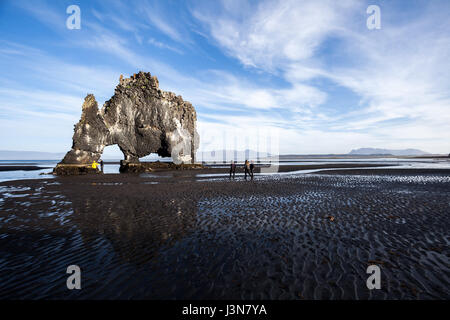 Landscape with rock gateat the beach. Light reflections in the water. Tough nature in Iceland at evening. Walking people. Stock Photo