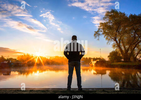 Rufford, Lancashire, 7th May 2017. UK Weather.  A man watches a beautiful sunrise & early morning mist as the sun tries to break through the clouds over the canal boats moored on Rufford Marina in Lancashire.  This local beauty spot is located just off the Leeds/Liverpool canal.  With it's stunning viewpoints and on site cafe's, it is a very popular resting place for those travelling this famous East to West route.  Credit: Cernan Elias/Alamy Live News Stock Photo