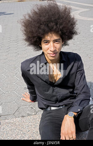 A twenty year old man dressed in all black with a large Afro hairdo. In Nuion Square Park in Manhattan, New York City. Stock Photo