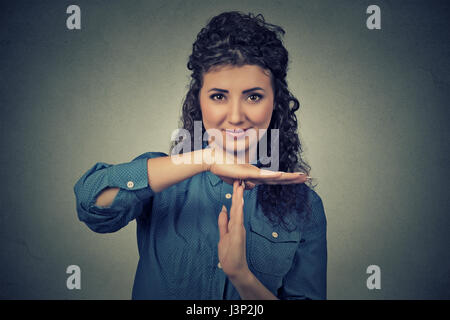 Closeup portrait, young, happy, smiling woman showing time out gesture with hands isolated on gray wall background. Positive human emotion facial expr Stock Photo