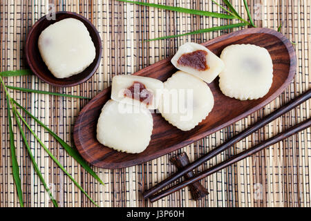 Mochi cake with red beans on wooden plate with bamboo leaves. Traditional Japanese dessert. Top view. Stock Photo