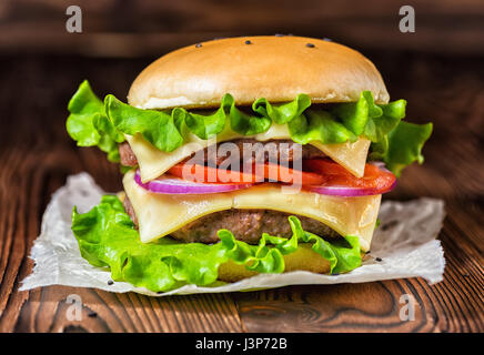 homemade full cheeseburger with vegetables, spices and beef meat on dark wooden background Stock Photo