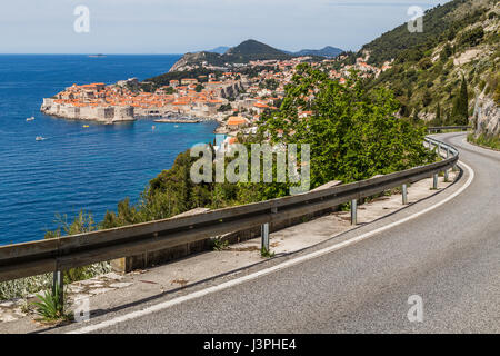 A winding single lane coastal road weaves along the side of steep limestone cliffs towards Dubrovnik. Stock Photo