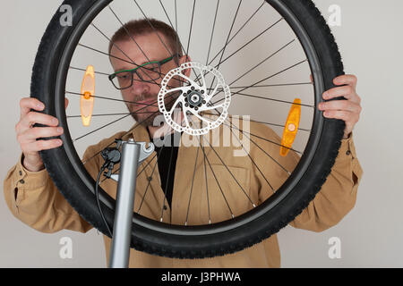 Bearded man puts the front wheel with hydraulic disc brake on the mtb bicycle. Stock Photo