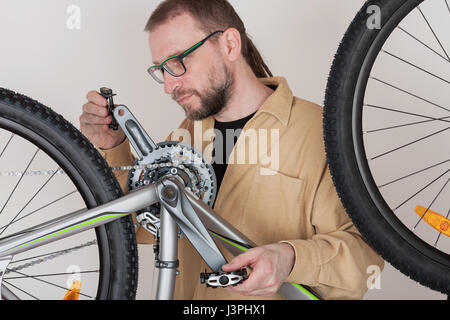Bearded man screws the pedals on the mtb bicycle. Stock Photo