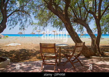 Terrace in the shade of Tamarisk trees, in the background straw parasols on a beach and a turquoise sea Stock Photo