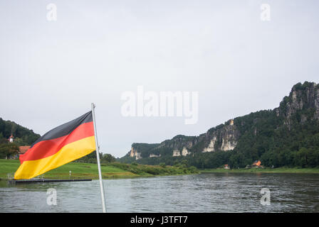 German flag at ferry through the Elbe at Kurort Rathen village and Bastei rocks at the background, Saxon Switzerland, Germany. Stock Photo