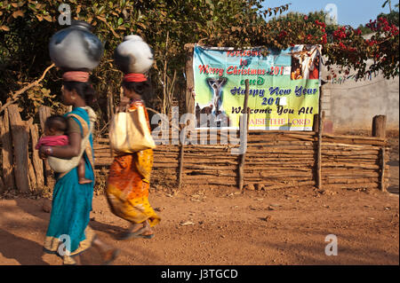 Two tribal women are walking in front of a poster celebrating christian festivities ( India) Stock Photo