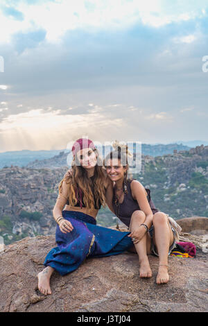 Two female backpackers sitting on a mountain in the sunset looking in the camera. Stock Photo