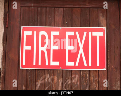 a big red and white sign outside on a fence saying fire exit Stock Photo