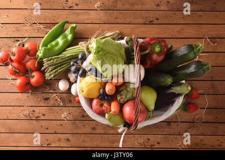 Assortment of fruits and vegetables in a wicker basket on a wooden table. Horizontal composition. Top view Stock Photo