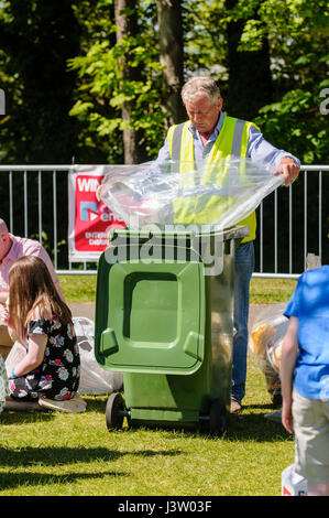 A council worker replaces the bin liner of a green wheelie waste bin at an outdoor event. Stock Photo