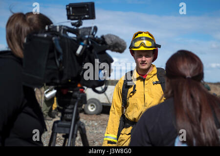 Local media reporters interview U.S. Air Force Senior Airman Grant Kopplin, a fire protection specialist assigned to the 673d Civil Engineer Squadron, during a controlled burn at the Infantry Platoon Battle Course on Joint Base Elmendorf-Richardson, Alaska, May 4, 2017. Controlled burns consume accumulated dry brush and grass thereby reducing the risk of wildfires. Kopplin is a native of Willard, Mo. (U.S. Air Force photo by Alejandro Pena) Stock Photo