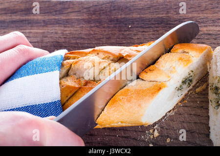 Cutting fresh bread on wooden board wrapped in towel Stock Photo