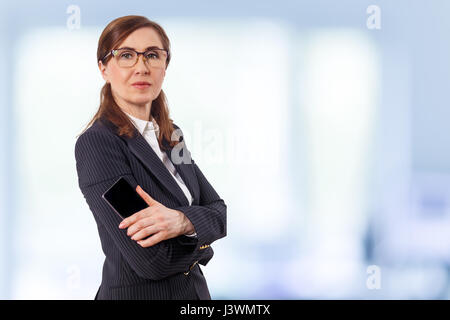 Portrait of a beautiful businesswoman 50 ears old with mobile phone in the office. Stock Photo