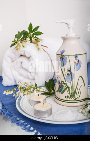 Lotion in an attractive pottery container, surrounded by Japonica, two tea candles and a bath towel Stock Photo