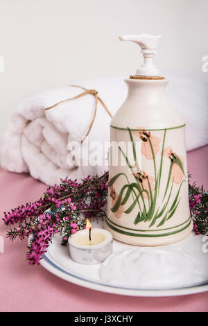 Lotion in an attractive pottery container, surrounded by heather (Erica darleyensis), a tea candle and a bath towel Stock Photo
