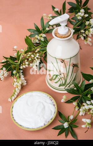 Lotion in an attractive pottery container, surrounded by white Lily of the Valley bush blossoms (Pieris japonica) in a studio setting Stock Photo