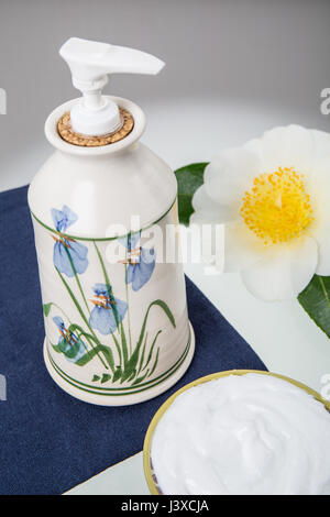 Lotion in an attractive pottery container surrounded by a bowl of lotion and a White Rugosa Rose blossom Stock Photo