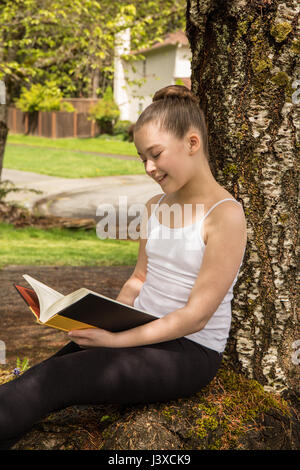 Eleven year old girl reading a book in the shade of a tree in Issaquah, Washington, USA Stock Photo
