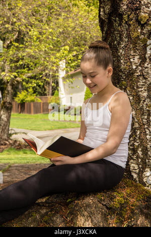 Eleven year old girl reading a book in the shade of a tree in Issaquah, Washington, USA Stock Photo