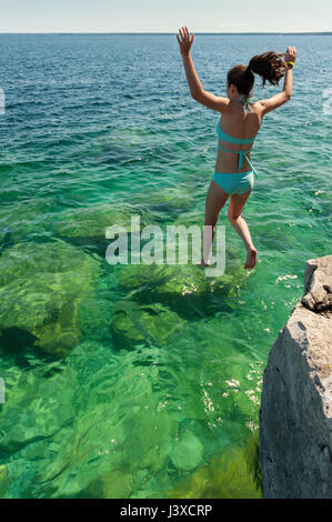 Summer, 16-19 year old teenager girl jumping in a lake from a cliff at Bruce Peninsula, Fathom Five National Marine Park, Tobermory, Ontario, Canada. Stock Photo