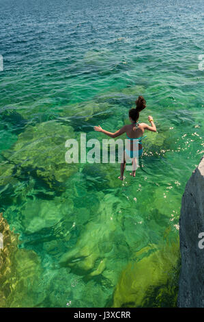 Summer, 16-19 year old teenager girl jumping in a lake from a cliff at Bruce Peninsula, Fathom Five National Marine Park, Tobermory, Ontario, Canada. Stock Photo